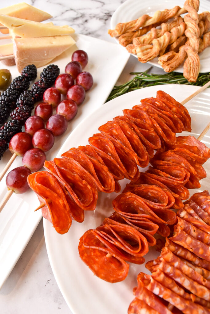 Making a meat bouquet with charcuterie skewers. Sliced cured meats and cheeses are pierced with wooden skewers and plated on a platter.