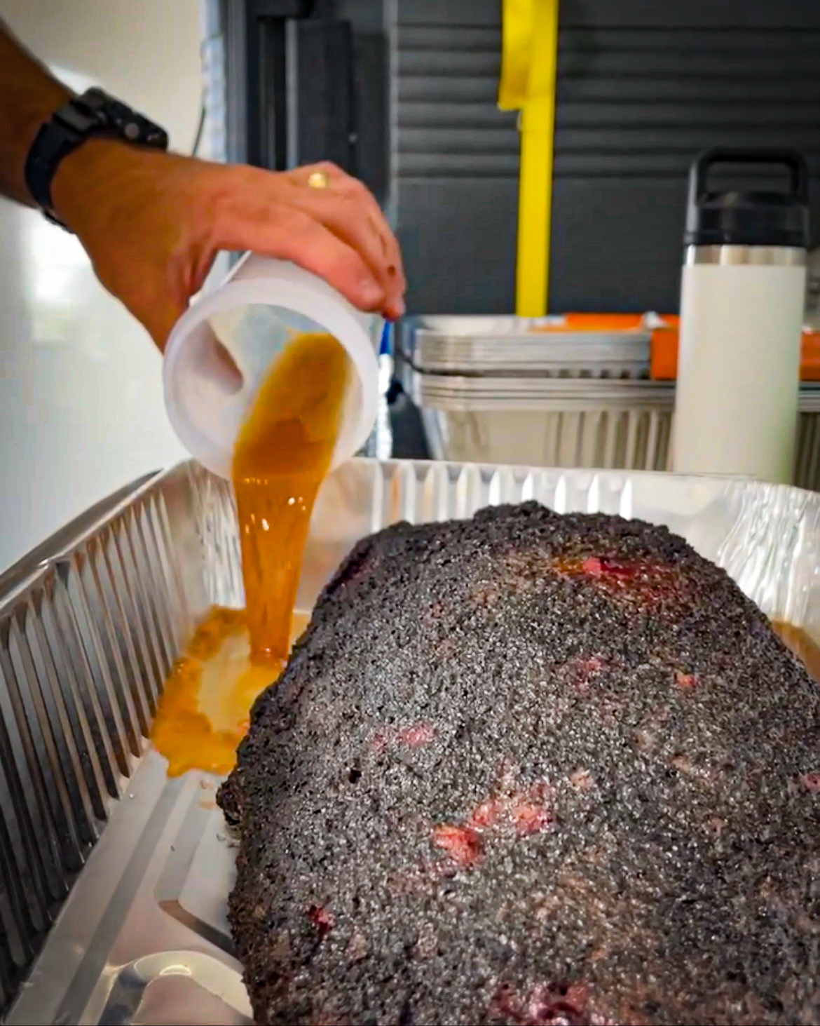 Adding liquid to an aluminum pan with brisket, also called the Texas crutch to get through the stall period.